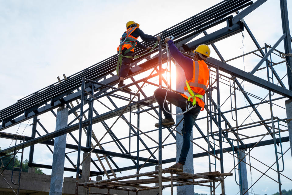 Construction worker wearing safety harness and safety line working on a metal roof.