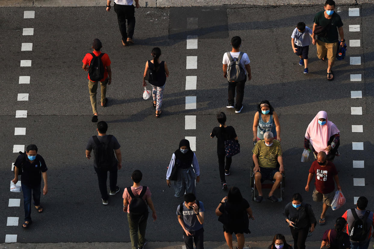 People wearing protective mask cross a street on June 8, 2021 in Singapore. Singapore enters a month long heightened alert from May 16 to June 13 to curb the spread of COVID-19 cases in the local community. New restrictions on movements and activities have been introduced such as limiting social interaction to two, prohibiting dining out and a reduced operating capacity at shopping malls, offices and attractions. (Photo by Suhaimi Abdullah/NurPhoto via Getty Images)