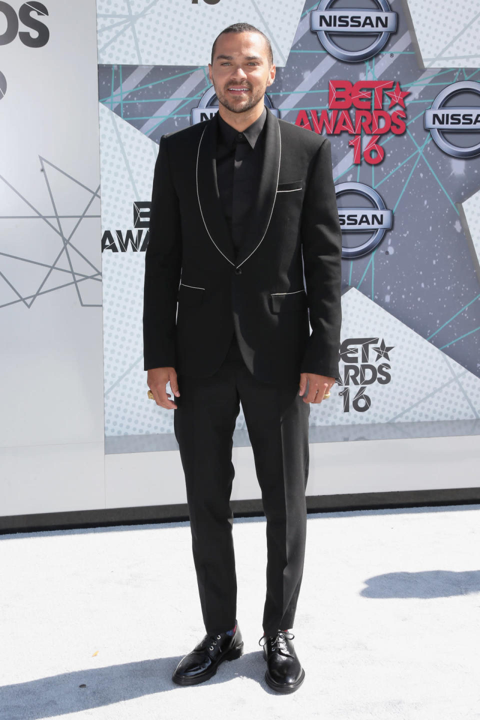 Jesse Williams in a black suit with white details 