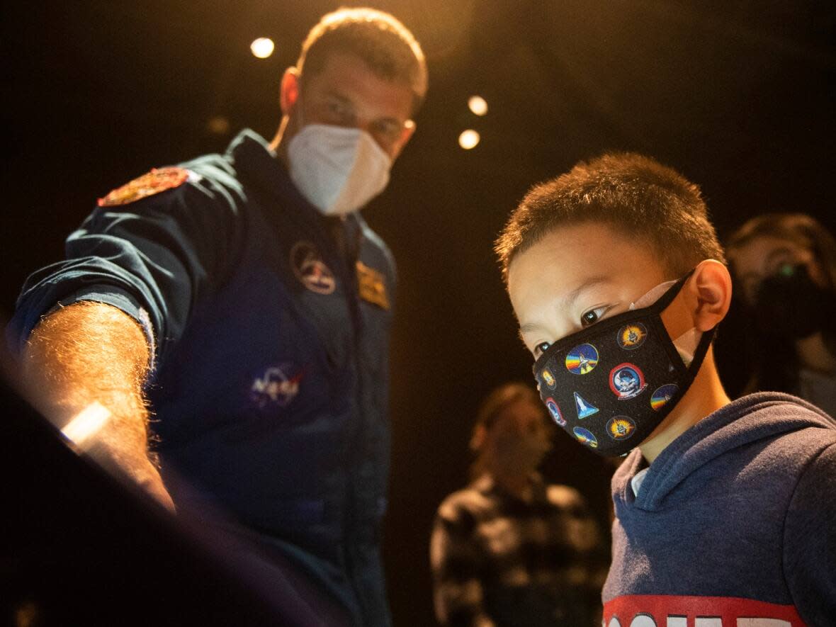 Albert Hsu, 8, wears a mask featuring space shuttle mission patches as he checks an interactive display with Canadian Space Agency astronaut Jeremy Hansen Nov. 26, 2021. The new exhibition Earth in Focus: Insights from Space is at the Canada Science and Technology Museum in Ottawa. (Justin Tang/Canadian Press - image credit)