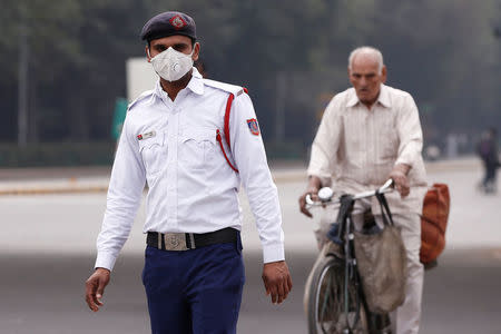 A traffic policeman wearing a mask to protect himself from dust and air pollution stands on a road-divider in New Delhi, India, February 6, 2018. REUTERS/Adnan Abidi