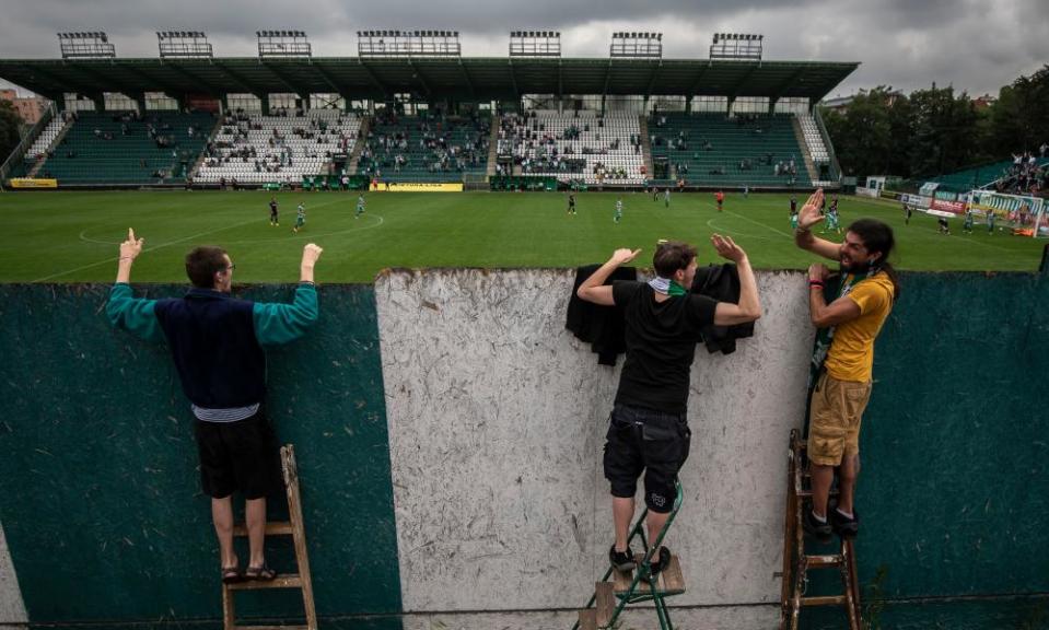 Fans stand on ladders to peer over a wall as they watch Bohemians 1905 in June.