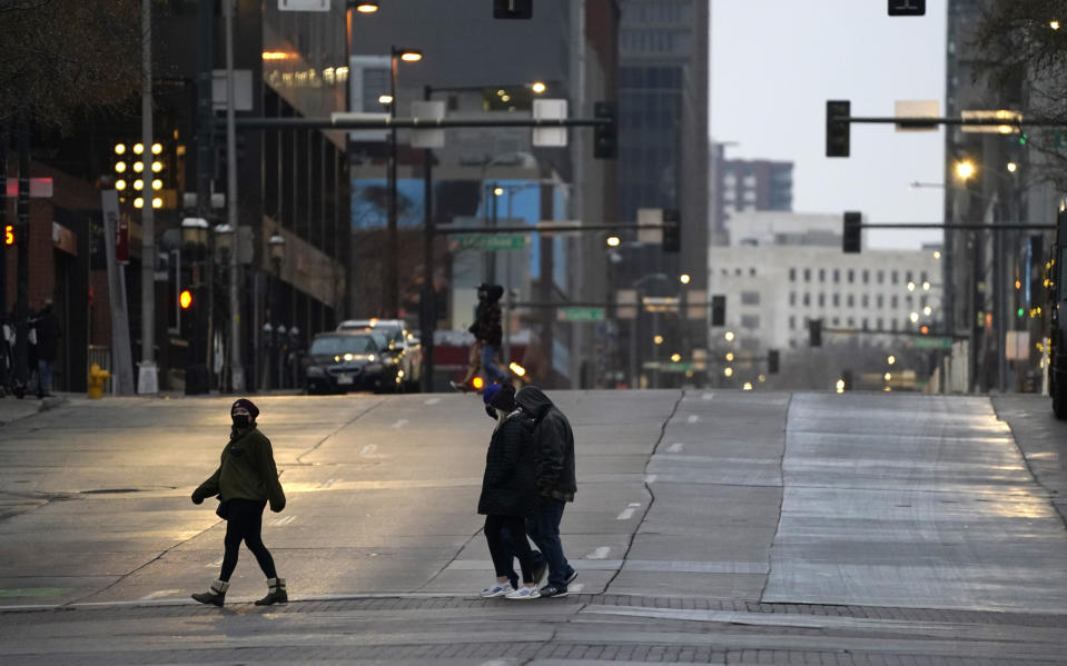 Pedestrians wear masks while crossing an empty road at the intersection of Market Street and 15th Avenue during the evening rush hour Monday, Dec. 28, 2020, in downtown Denver. (AP Photo/David Zalubowski)