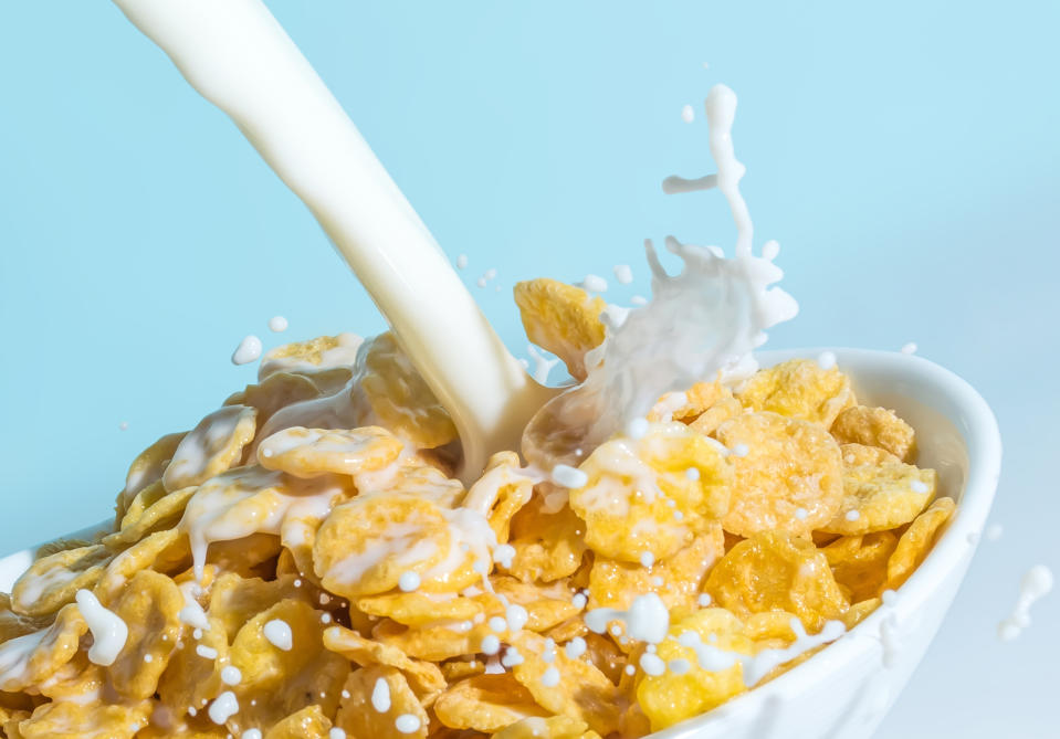 Ein Milchstrahl trifft auf Müsli Cornflakes in einer Schüssel, Milch spritzt aus Müslischale