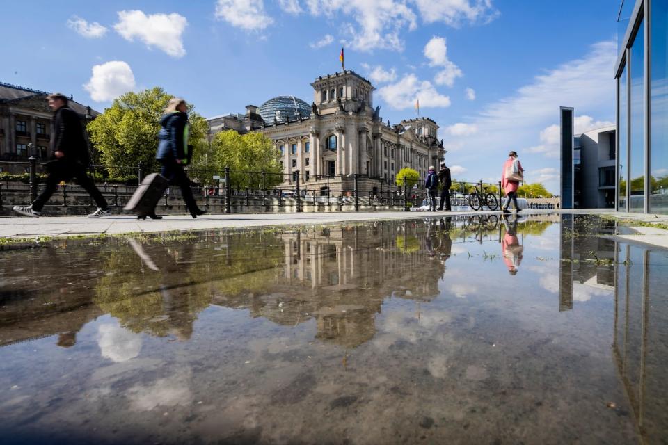 People walk past Reichstag building while being reflected in a puddle in Berlin, Germany, Tuesday, April 23, 2024. 