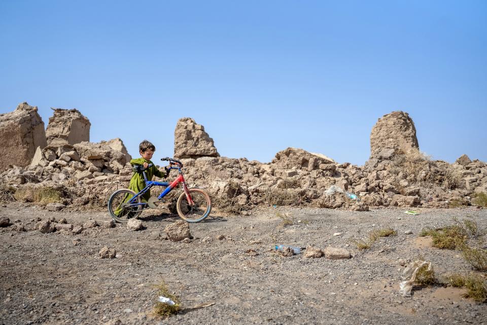 A boy wheels his bike past the devastated remains of his village in western Afghanistan.