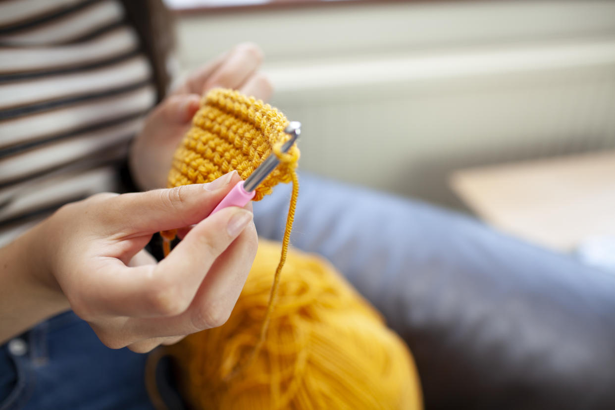  A woman crochets an item using bright yellow yarn. 