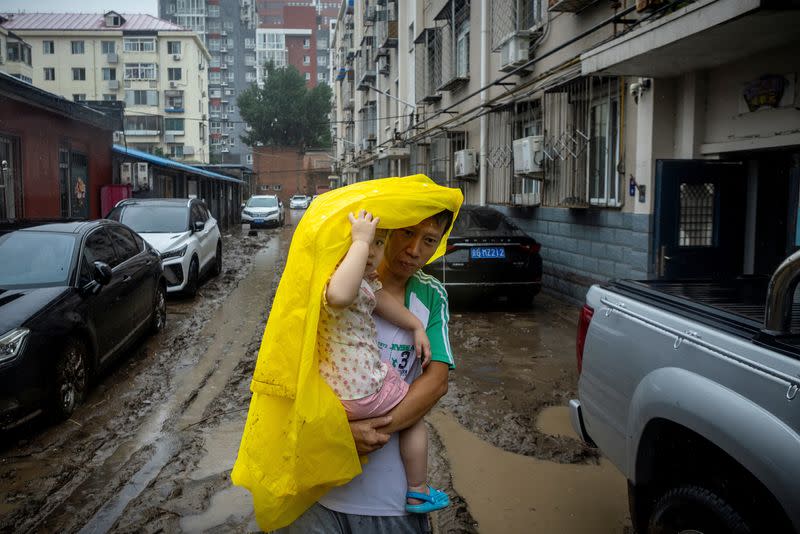 A man carries a child through the mud after floods, in a neighbourhood affected by days of heavy rain from remnants of Typhoon Doksuri, in Beijing