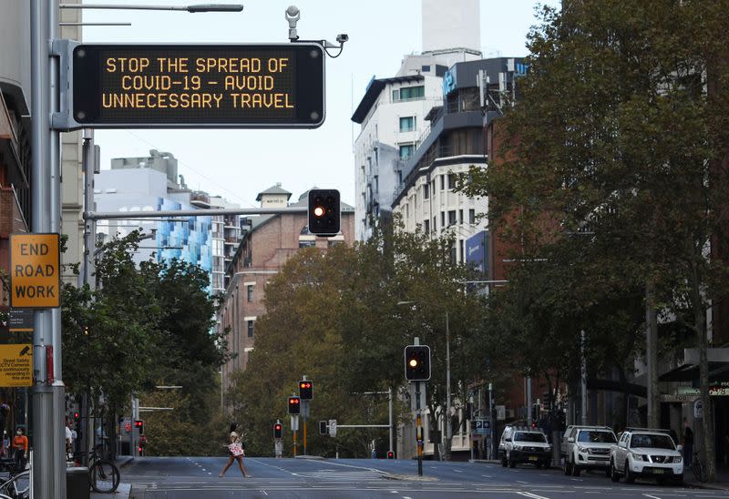 A woman crosses an almost empty street near of a coronavirus warning sign during a workday following the implementation of stricter social-distancing and self-isolation rules to limit the spread of the coronavirus disease (COVID-19) in Sydney