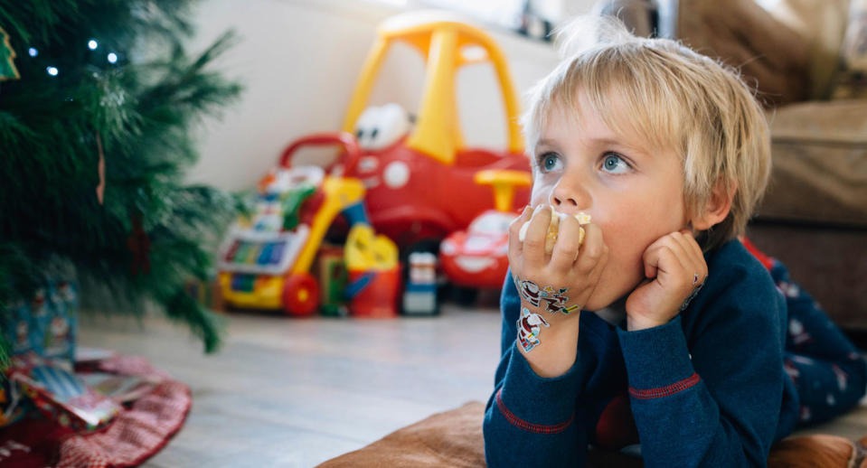 A little boy eats popcorn next to a Christmas tree.