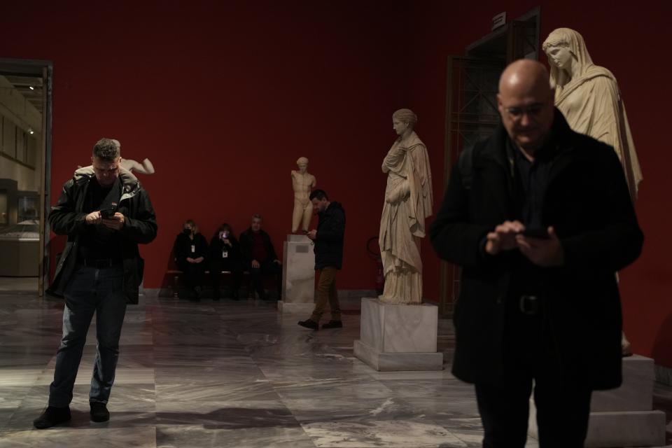 People check their cellphones among statues during the presentation event for the planned renovation of the National Archaeological Museum in Athens, Greece, on Wednesday, Feb. 15, 2023. The British architect, David Chipperfield, is leading the project that will expand the museum's exhibition space, create a new entrance, and garden space. The museum, which showcases artifacts from ancient Greece, is considered to be one of the most important in the world. (AP Photo/Thanassis Stavrakis)