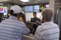 Lawrence Cheng, center, whose family owns seven Wendy's locations south of Los Angeles, takes orders from customers at his Wendy's restaurant in Fountain Valley, Calif., June 20, 2024. California's minimum wage increase that went into effect in April and saw fast food workers across the state go from making $16 to $20 overnight is already having an impact. "We kind of just cut where we can," said Cheng. "I schedule one less person, and then I come in for that time that I didn't schedule, and I work that hour." (AP Photo/Jae C. Hong)