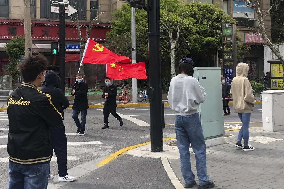 FILE - Residents hold up the Communist Party flag and the Chinese national flag as others prepare to take part in the first round of mass COVID tests in the Jingan district of western Shanghai, China, on April 1, 2022. Shanghai's lockdown is an abrupt about-face from just a month ago, when some Chinese health experts publicly suggested softening pandemic control measures. (AP Photo/Chen Si, File)