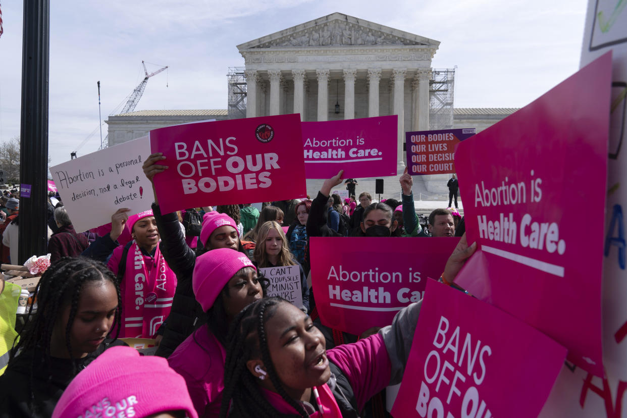 Dozens of protesters in front of what appears to be the Supreme Court building wear pink and hold pink signs reading: Bans off our bodies and Abortion is health care.