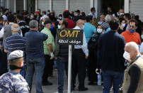 Lebanese citizens wear mask and gloves to help curb the spread of the coronavirus, outside a Western Union shop to receive their money transfer in U.S. dollar currency, during the last day that they are allowed to dispense dollars to customers following new Central Bank rules, in Beirut, Lebanon, Thursday, April 23, 2020. Lebanon's currency continued its downward spiral before the dollar on Thursday, reaching a new low amid financial turmoil in the crisis-hit country. (AP Photo/Hussein Malla)
