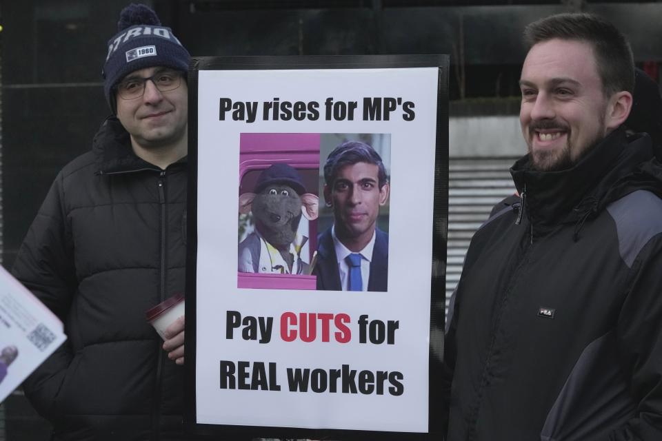 FILE - Rail workers hold up a sign with pictures of a television puppet character Roland Rat, left, and British Prime Minister Rishi Sunak during a strike outside Euston station in London, Feb. 1, 2023. British Prime Minister Rishi Sunak marks 100 days as U.K. prime minister on Thursday, Feb. 2 – more than twice the number achieved up by his ill-fated predecessor, Liz Truss. But the leader who calmed financial markets after Truss' disastrous economic plans now faces a host of challenges, from double-digit inflation and a wave of strikes to ethics scandals in the governing Conservative Party. (AP Photo/Kin Cheung, file)