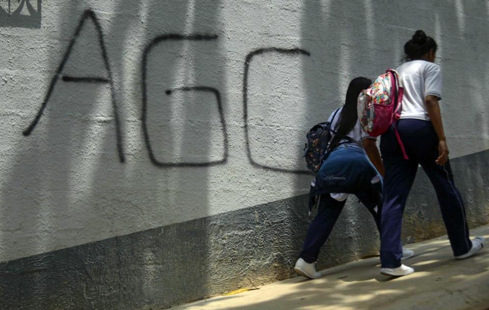 Estudiantes caminan junto a un muro que luce un grafiti con las iniciales AGC (Autodefensas Gaitanistas de Colombia), nombre con el que se autodenonima el Clan del Golfo, el 1 de abril de 2016 en Medellín (AFP | RAUL ARBOLEDA)