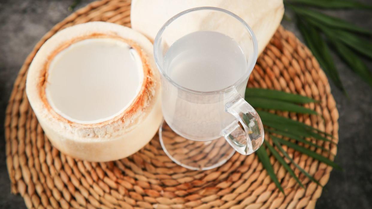 open coconut and a glass of coconut milk on a woven placemat