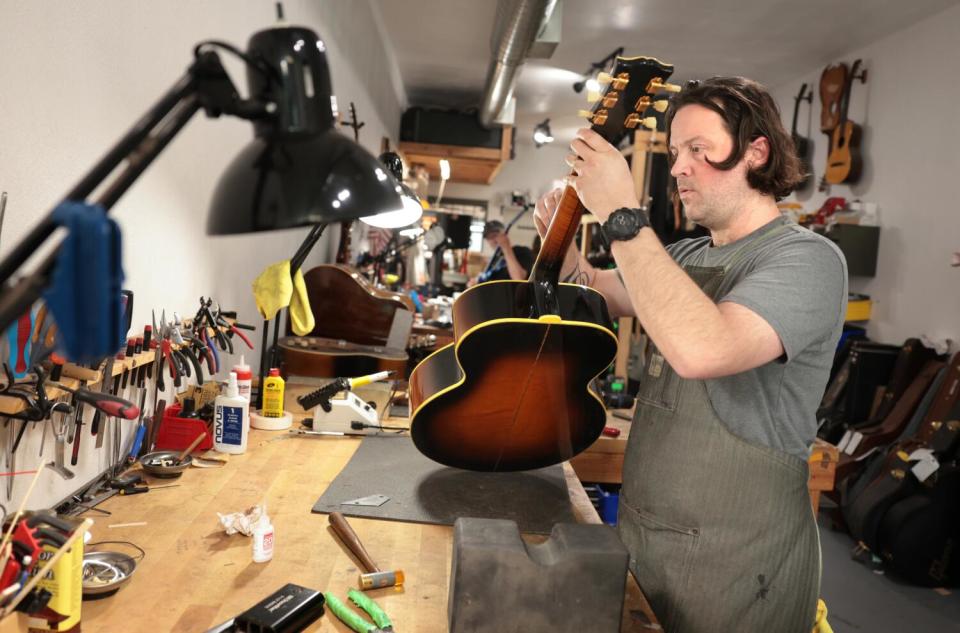 A man sits in a workshop playing an acoustic guitar