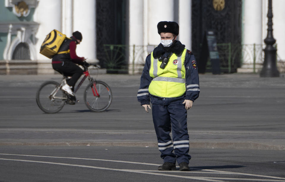 A food delivery courier rides a bike past a road police officer wearing face mask, to protect against coronavirus, in St.Petersburg, Russia, Tuesday, March 31, 2020. Moscow, the country's capital, and more than 30 Russian regions have been on lockdown since Monday, with most businesses closed and residents not allowed to leave their apartments except for grocery shopping, buying medicines, taking out trash or walking their dogs. The new coronavirus causes mild or moderate symptoms for most people, but for some, especially older adults and people with existing health problems, it can cause more severe illness or death. (AP Photo/Dmitri Lovetsky)