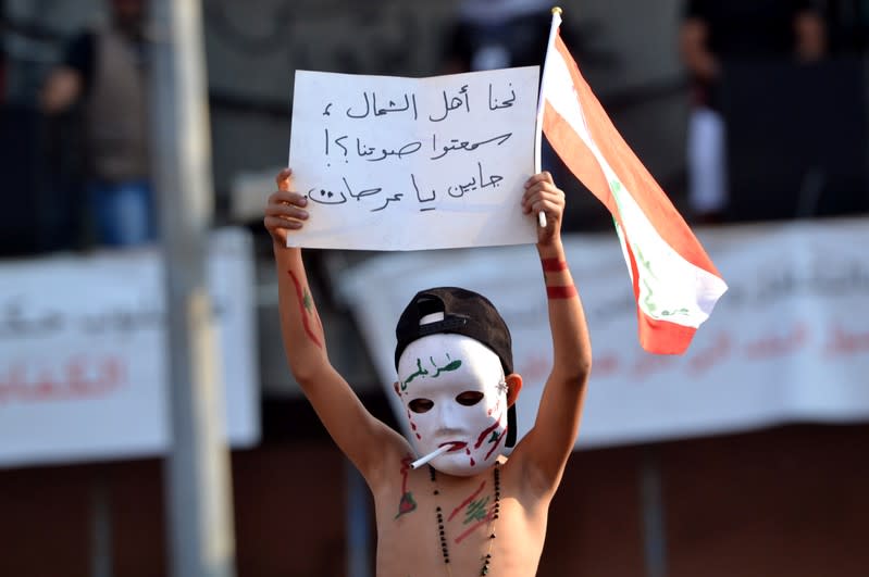 A child wears a mask and holds a sign during an anti-government protest in Tripoli