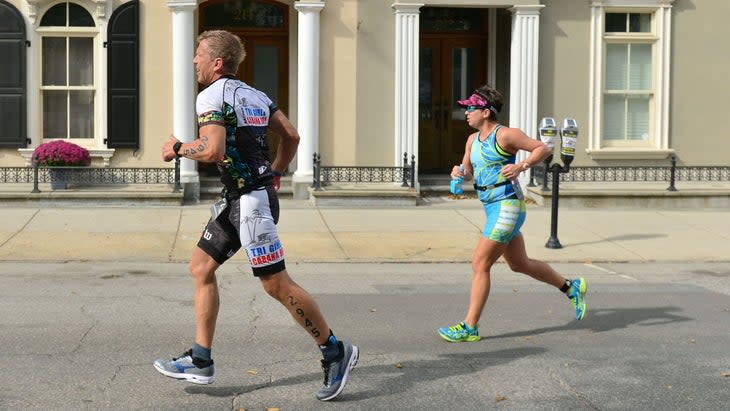 Two triathletes, a male and a female, run in triathlon clothing.