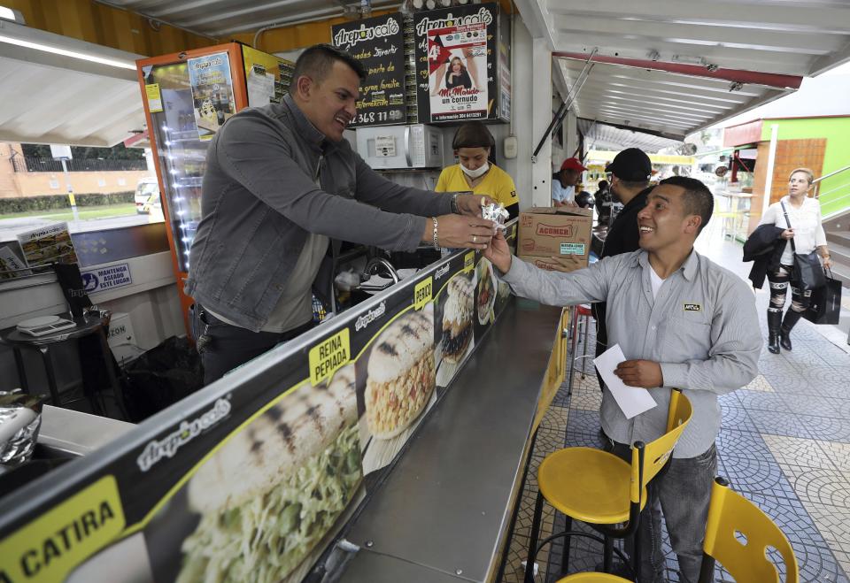 In this June 11, 2019 photo, Gerson Briceno, owner of the fast food restaurant "Arepas Cafe" serves a customer in Bogota, Colombia, Tuesday, June 11, 2019. Today, Arepas Café has nine locations around Bogotá. "I always missed the flavor of home," he said. (AP Photo/Fernando Vergara)