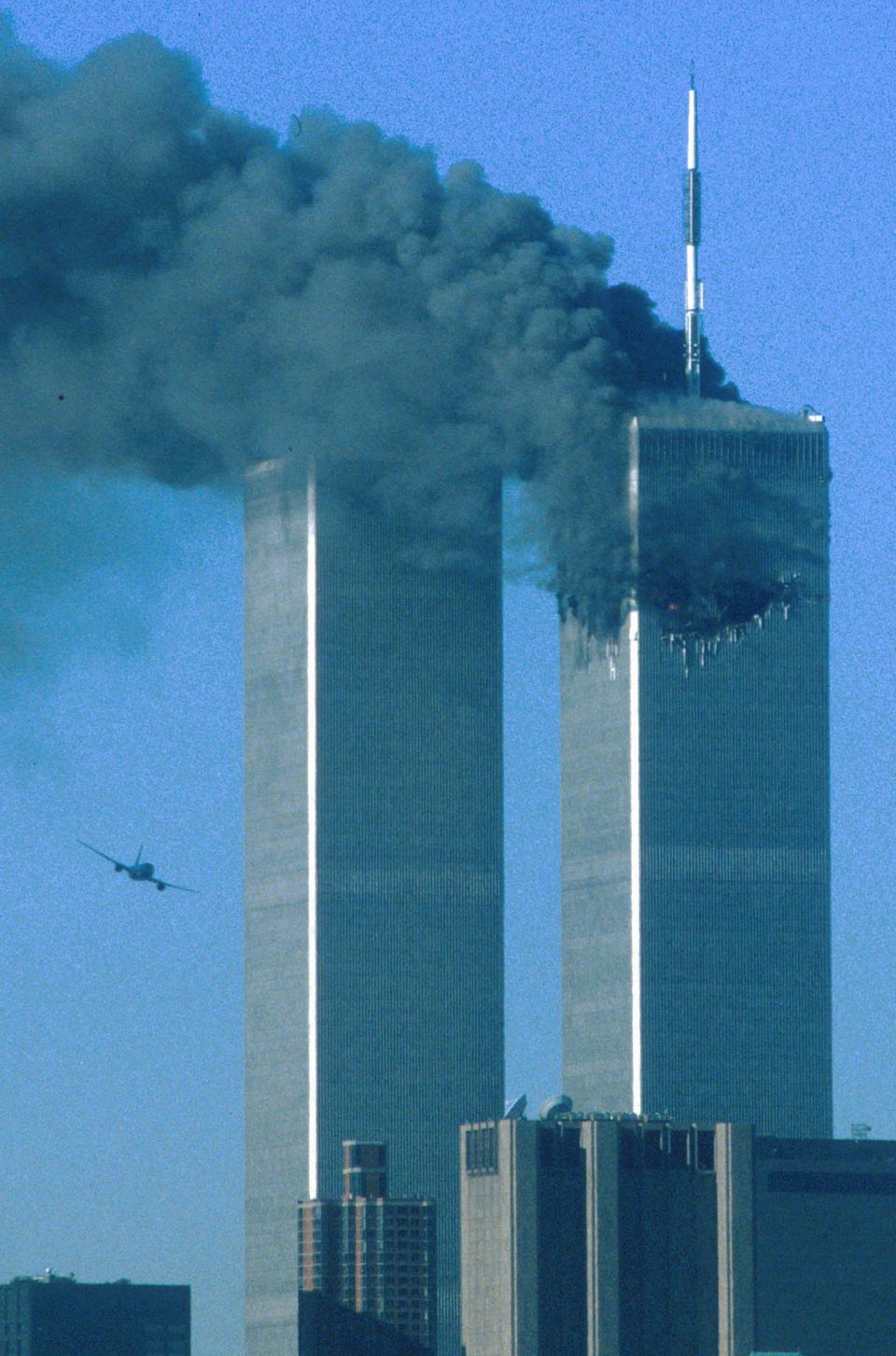 The hijacked United Airlines Flight 175 flies toward the Twin Towers of the World Trade Center shortly before crashing into the South Tower, while the North Tower burns following an earlier attack by a hijacked plane in New York City on September 11, 2001.