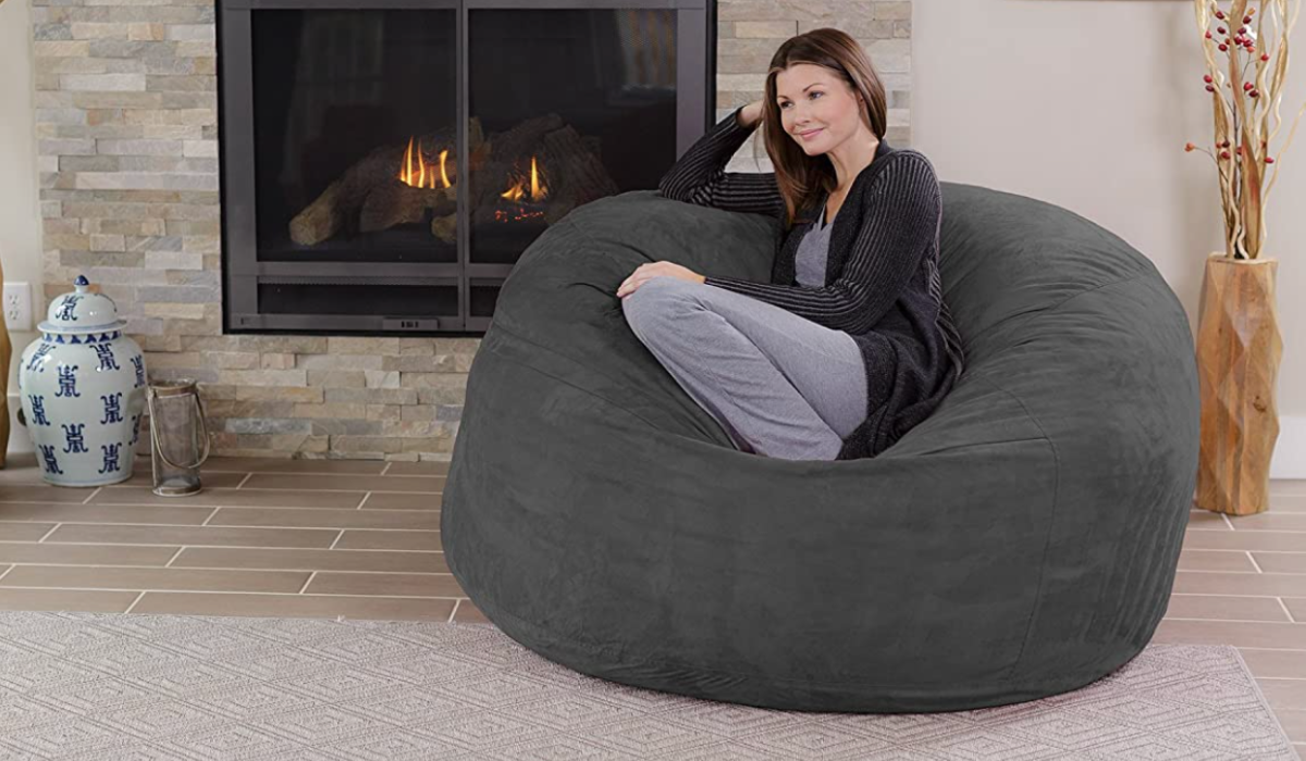 A woman sitting on oversized grey bean bag chair in front of fireplace.