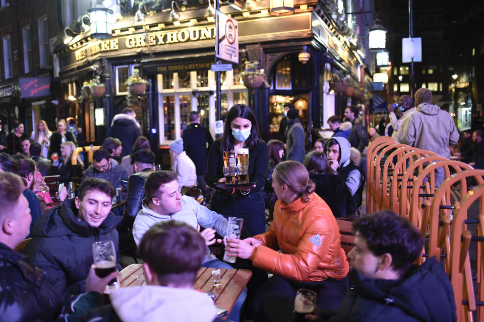 A waitress serves drinks as customers sit at setup tables outside pubs in Soho, in London, on the day some of England's third coronavirus lockdown restrictions were eased by the British government, Monday, April 12, 2021. People across England flocked to shed shaggy locks and browse for clothes, books and other "non-essential" items as shops, gyms, hairdressers, restaurant patios and beer gardens reopened Monday after months of lockdown. (AP Photo/Alberto Pezzali)