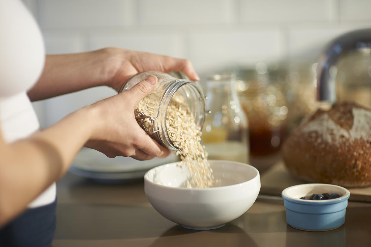 Close up of a woman preparing a wholesome breakfast by pouring oats into a bowl from a plastic free jar with fresh berries.