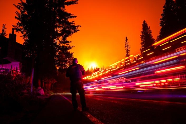 A man stands on the shoulder of a road as a vehicle streaks by in a long exposure.