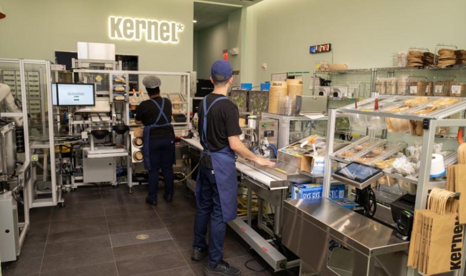 Two Kernel workers are standing in the kitchen's assembly line.