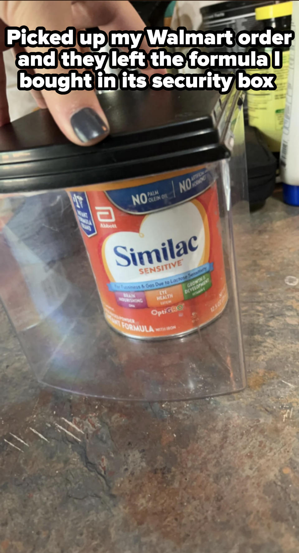 Person's hand lifting a Similac Sensitive infant formula can from a container on a countertop