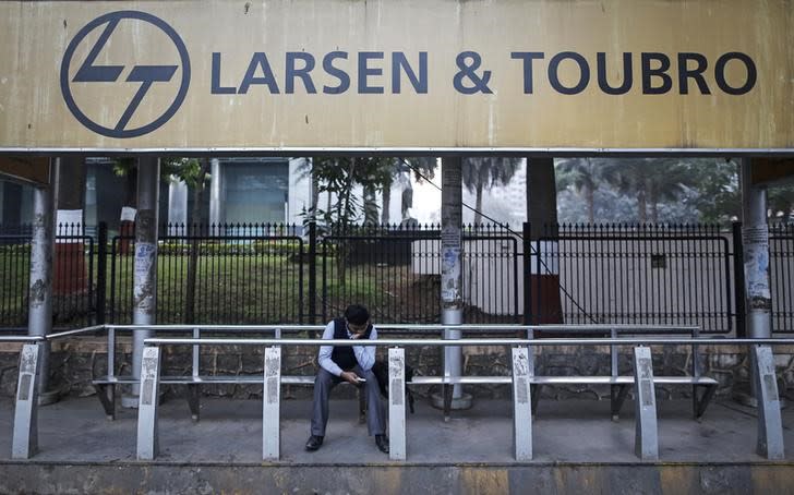 A man waits at a bus-stop with an advertisement of Larsen & Toubro outside the company's manufacturing unit in Mumbai January 22, 2014. REUTERS/Danish Siddiqui/Files