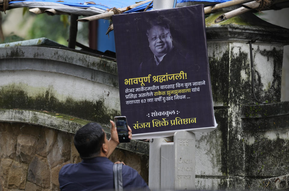 A man takes picture of a poster paying homage to veteran stock market investor and Indian billionaire Rakesh Jhunjhunwala displayed outside his residence, in Mumbai, India, Sunday, Aug.14, 2022. Jhunjhunwala, nicknamed India’s own Warren Buffett, died Sunday in Mumbai city, Press Trust of India news agency reported. He was 62. (AP Photo/Rafiq Maqbool)