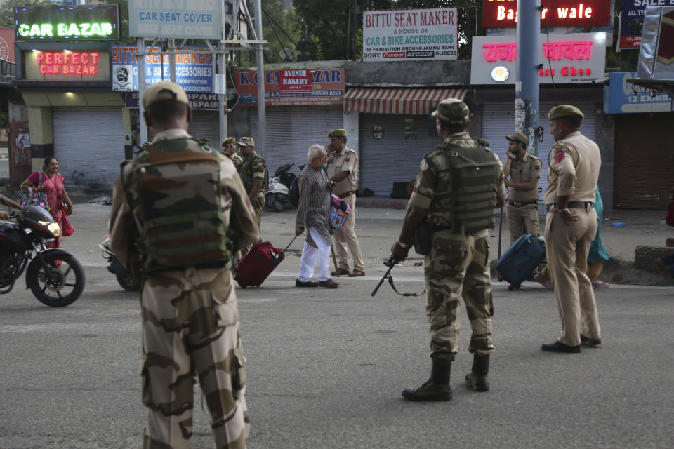 Tourists walk past Indian security forces during curfew like restrictions in Jammu, India, Monday, Aug. 5, 2019. An indefinite security lockdown was in place in the Indian-controlled portion of divided Kashmir on Monday, stranding millions in their homes as authorities also suspended some internet services and deployed thousands of fresh troops around the increasingly tense region. (AP Photo/Channi Anand)