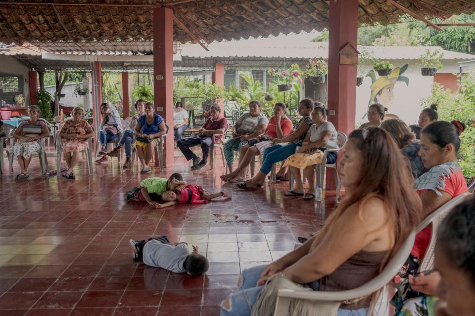 Adults sit around in a circle as kids lie about in the middle.