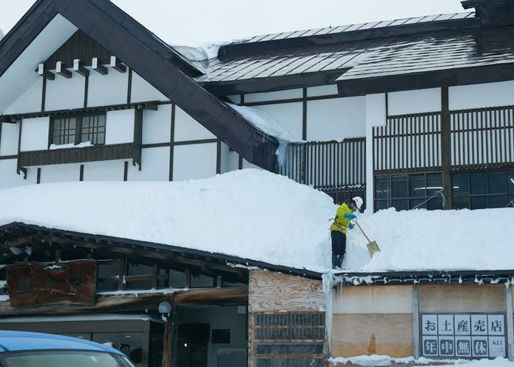 繫著安全帶將屋頂上的雪掃下來的身姿