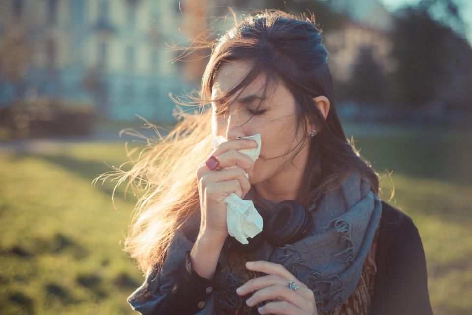 mid adult woman blowing nose with hankerchief in park