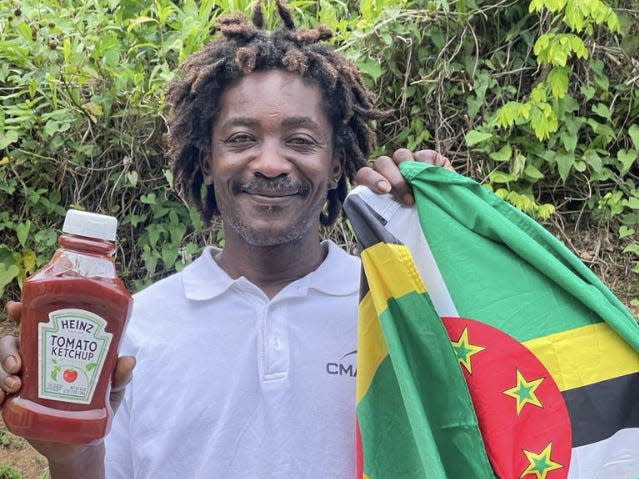 Photo of Elvis Francois smiling whilst holding a ketchup bottle and Dominica flag