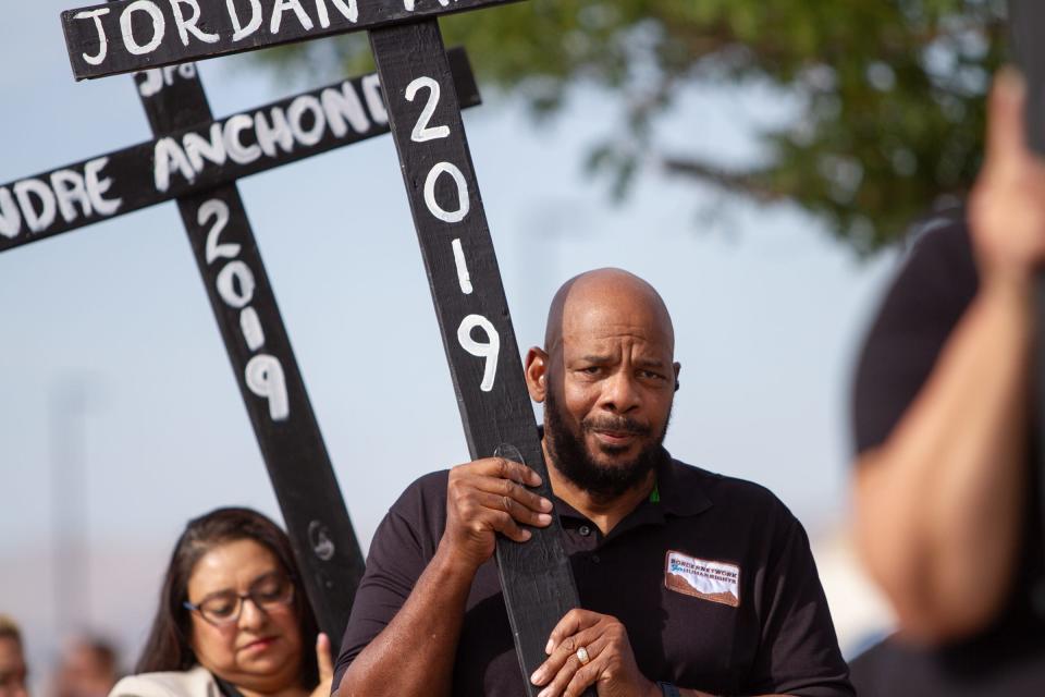 Rev. Micheal Grady from the Prince of Peace Christian Fellowship church carries a cross with the name Jordan Anchondo who died alongside his wife, Andre Anchondo, protecting their child inside a Walmart in El Paso, Texas, during a mass shooting on Aug. 3. 2019. The vigil was held on the fourth anniversary of the mass shooting in Ponder Park on Aug. 3, 2023.