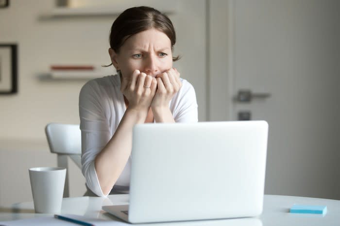 A woman puts her hands to her mouth in worry as she looks at her laptop screen.