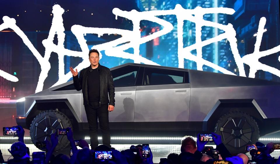 Tesla CEO Elon Musk stands in front of a Cybertruck on a stage in front of a crowd at a presentation.