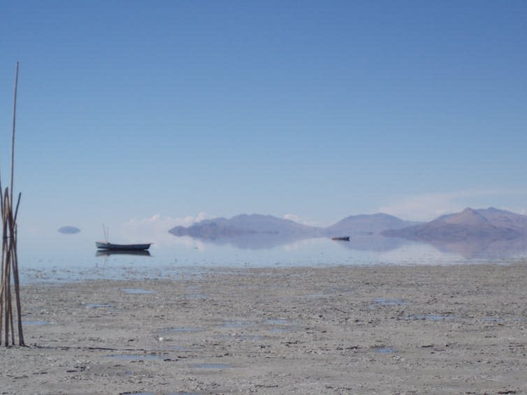 Dried shore, boats on lake, hills in distance.