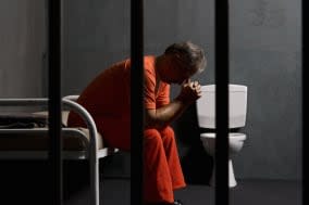 A prisoner sitting on a bed in a prison cell