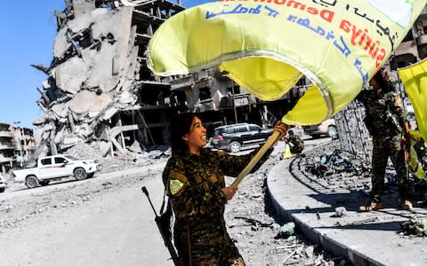 Rojda Felat, a Syrian Democratic Forces (SDF) commander, waves her group's flag at the iconic Al-Naim square in Raqqa  - Credit: AFP