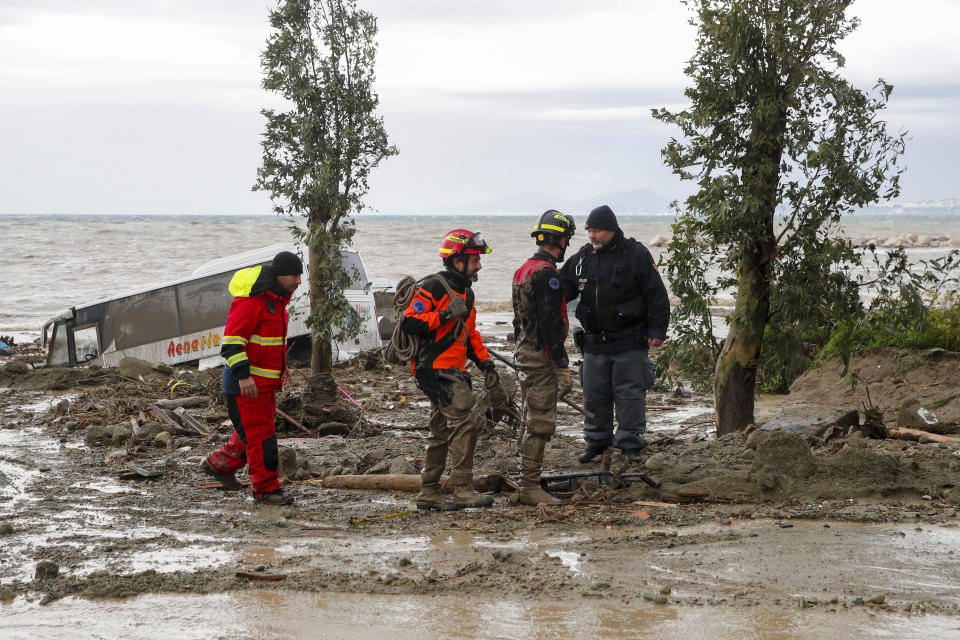 Rescuers stand next to a bus carried away after heavy rainfall triggered landslides that collapsed buildings and left as many as 12 people missing, in Casamicciola, on the southern Italian island of Ischia, Saturday, Nov. 26, 2022. Firefighters are working on rescue efforts as reinforcements are being sent from nearby Naples, but are encountering difficulties in reaching the island either by motorboat or helicopter due to the weather. (AP Photo/Salvatore Laporta)