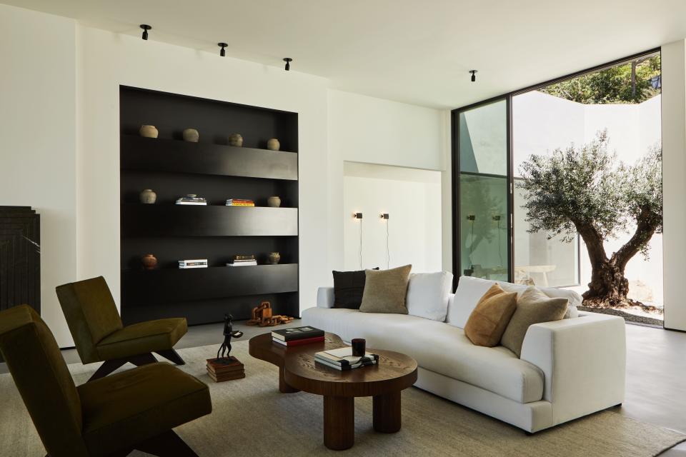 The upholstered sofa in white Belgian linen from Harbour and Pierre Jeanneret chairs reupholstered in Cavallini olive pony hair from Edelman sit on a silver wool Soumak rug from Lawrence of La Brea and surround a custom coffee table by OSKLO.