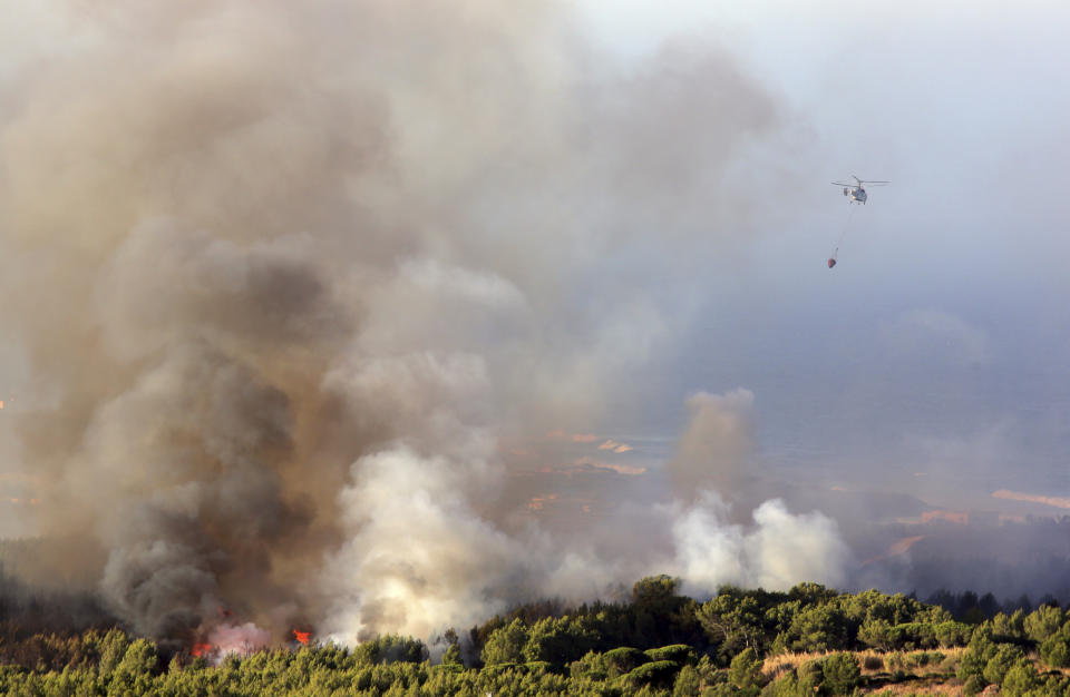 A firefighting helicopter flies above a forest fire burning at sunrise near the village of Charneca, in the Sintra national park, west of Lisbon, Sunday, Oct. 7, 2018. Over 700 firefighters were battling a forest fire that started overnight about 40 kilometers (25 miles) west of Lisbon. (AP Photo/Armando Franca)